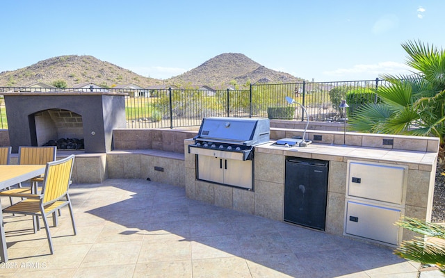 view of patio / terrace featuring exterior fireplace, a mountain view, area for grilling, fence, and exterior kitchen