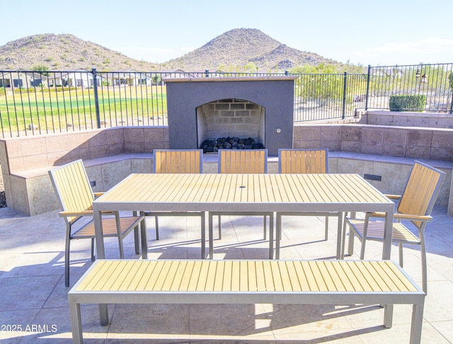 view of patio with exterior fireplace, outdoor dining area, fence, and a mountain view