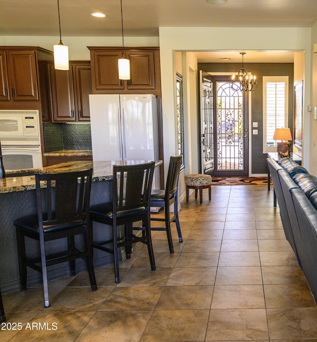 kitchen with a breakfast bar, pendant lighting, decorative backsplash, dark stone countertops, and white appliances