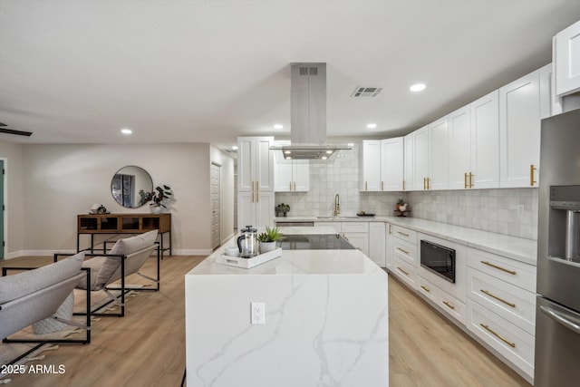 kitchen with white cabinetry, black microwave, island range hood, and stainless steel fridge