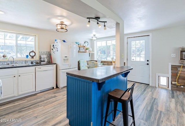 kitchen featuring white appliances, sink, hardwood / wood-style floors, white cabinetry, and a breakfast bar