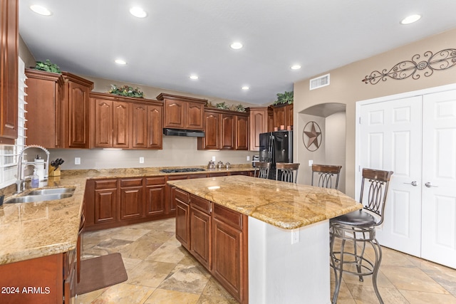 kitchen with black fridge, a center island, sink, a breakfast bar area, and light stone counters