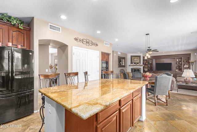 kitchen with ceiling fan, pendant lighting, a kitchen island, black fridge with ice dispenser, and a breakfast bar area