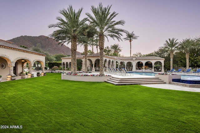 pool at dusk featuring a lawn and a mountain view