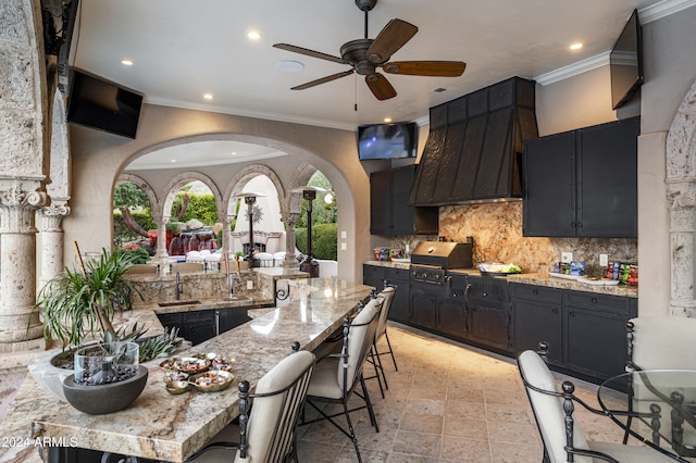 kitchen featuring a kitchen bar, light stone countertops, tasteful backsplash, ceiling fan, and sink