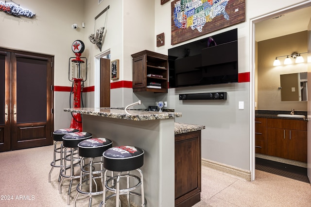 kitchen with dark brown cabinets, light stone counters, a breakfast bar area, and sink