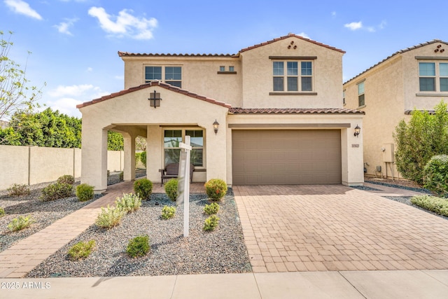mediterranean / spanish-style home with a tile roof, decorative driveway, an attached garage, and stucco siding