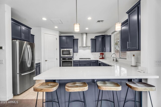 kitchen with visible vents, a peninsula, wall chimney exhaust hood, appliances with stainless steel finishes, and a sink