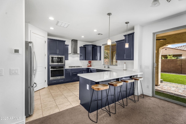 kitchen with visible vents, a peninsula, a breakfast bar, wall chimney exhaust hood, and stainless steel appliances