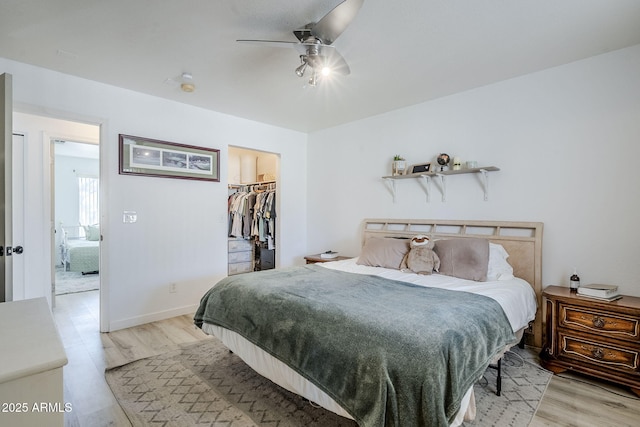 bedroom featuring a walk in closet, light hardwood / wood-style floors, a closet, and ceiling fan