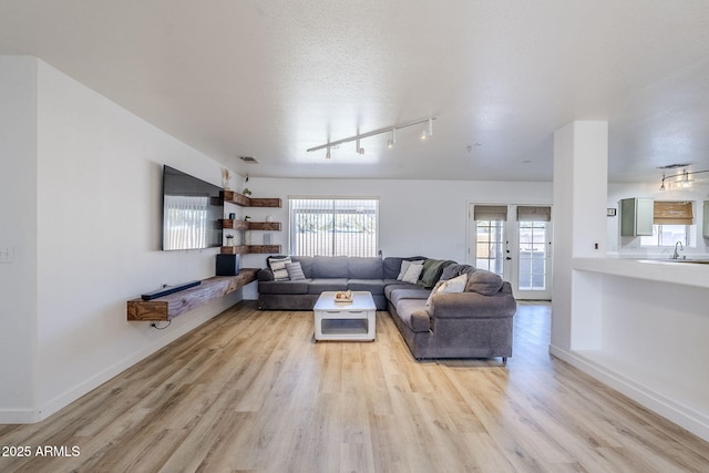 living room featuring sink, light wood-type flooring, track lighting, a textured ceiling, and french doors