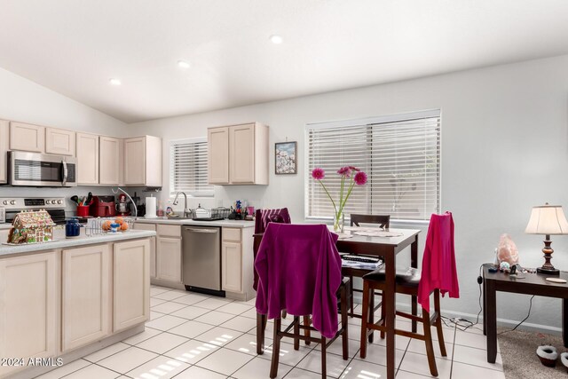 kitchen featuring stainless steel appliances, sink, cream cabinetry, lofted ceiling, and light tile patterned flooring