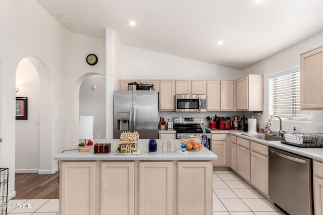 kitchen with sink, a kitchen island, vaulted ceiling, light tile patterned floors, and appliances with stainless steel finishes