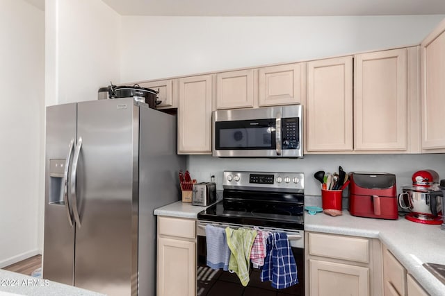 kitchen with appliances with stainless steel finishes, hardwood / wood-style flooring, vaulted ceiling, and light brown cabinetry