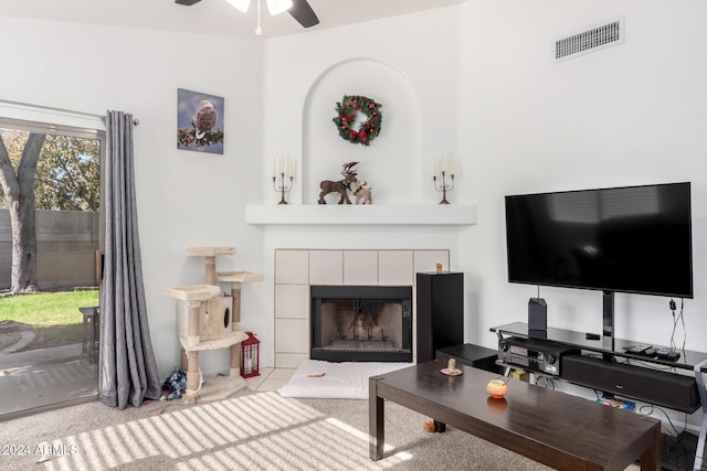 living room featuring a tiled fireplace, ceiling fan, and light colored carpet