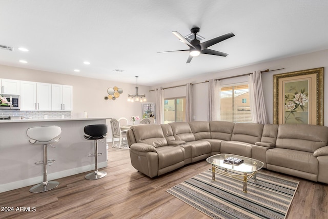 living room featuring ceiling fan with notable chandelier and light wood-type flooring