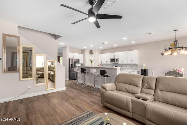 living room with ceiling fan with notable chandelier and light hardwood / wood-style flooring