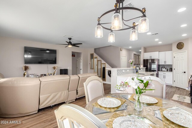 dining room with light wood-type flooring, ceiling fan with notable chandelier, and sink