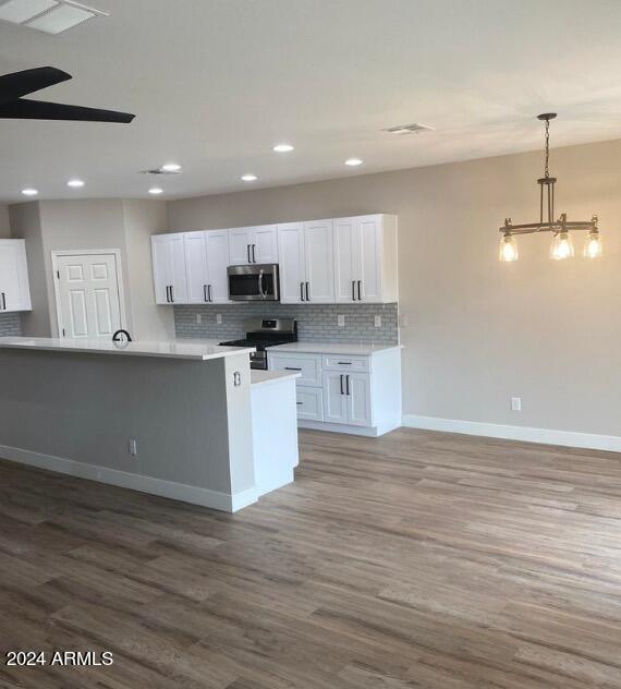 kitchen with wood-type flooring, white cabinetry, hanging light fixtures, and appliances with stainless steel finishes