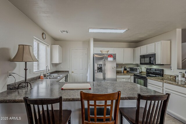 2125 W Central Ave, Coolidge, AZ 85128 - kitchen with black appliances, a peninsula, a breakfast bar, dark countertops, and white cabinetry