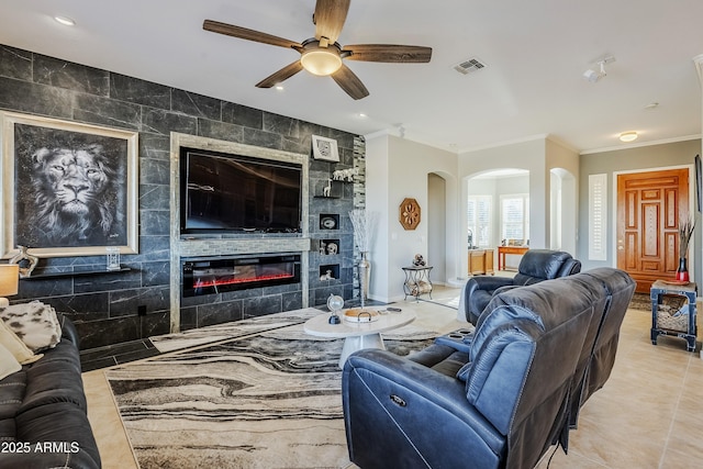 living room featuring a tile fireplace, tile walls, ceiling fan, and crown molding