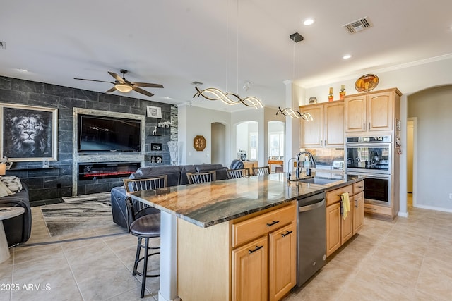 kitchen with sink, decorative light fixtures, stainless steel appliances, and an island with sink