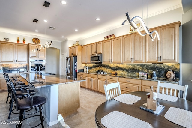 kitchen with stainless steel appliances, an island with sink, hanging light fixtures, and backsplash