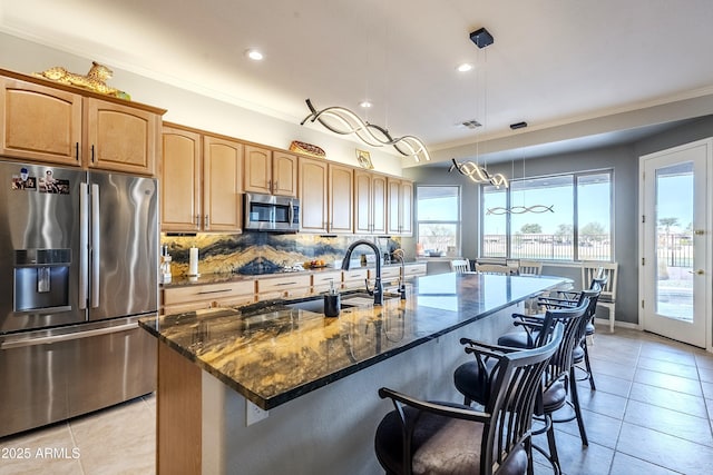 kitchen with light tile patterned floors, dark stone countertops, pendant lighting, stainless steel appliances, and a kitchen island with sink