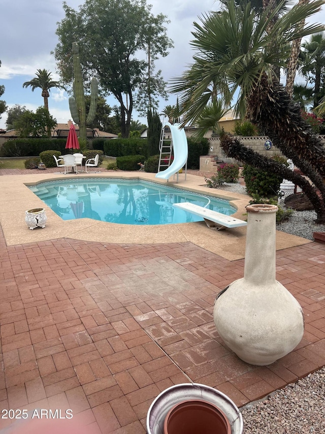 swimming pool featuring a diving board, a water slide, and a patio