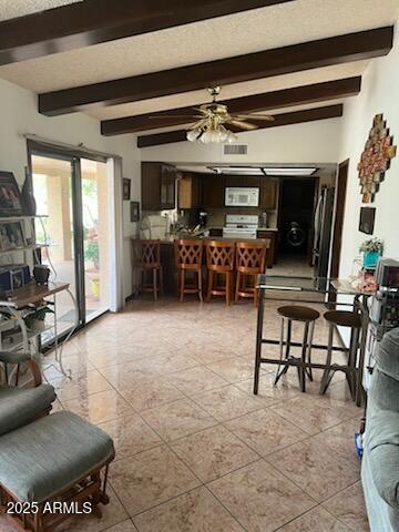 living area with light tile patterned floors, a ceiling fan, and beam ceiling