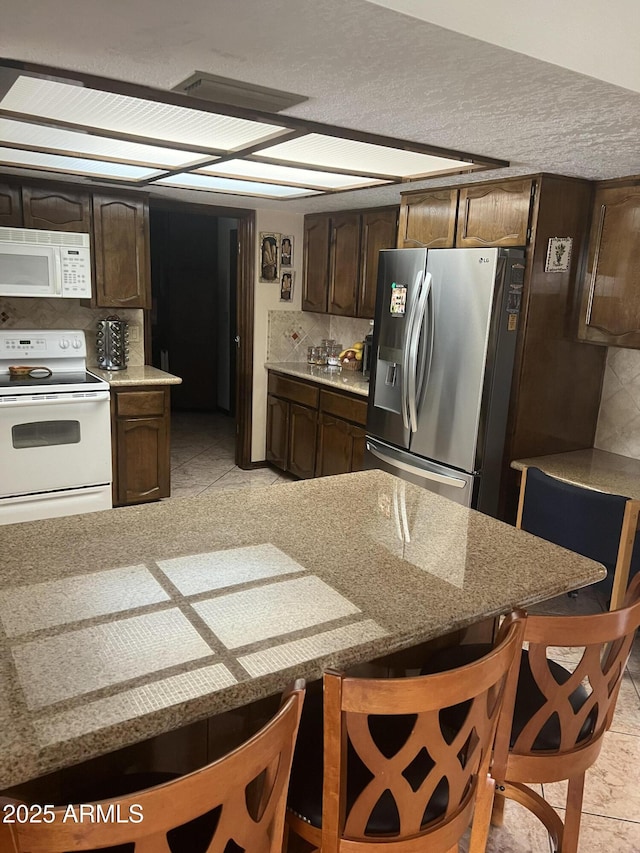 kitchen featuring white appliances, dark brown cabinets, tasteful backsplash, and light stone counters