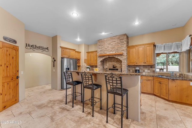 kitchen featuring a center island, stainless steel refrigerator with ice dispenser, decorative backsplash, stone countertops, and a breakfast bar