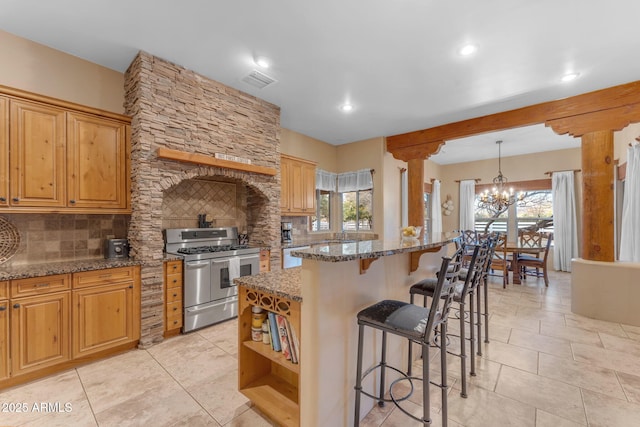 kitchen featuring an inviting chandelier, tasteful backsplash, range with two ovens, stone countertops, and a kitchen island