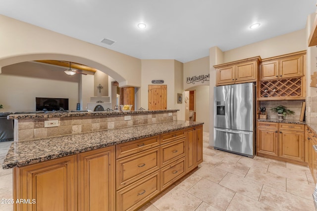 kitchen featuring stainless steel fridge with ice dispenser, ceiling fan, decorative backsplash, dark stone counters, and a kitchen island