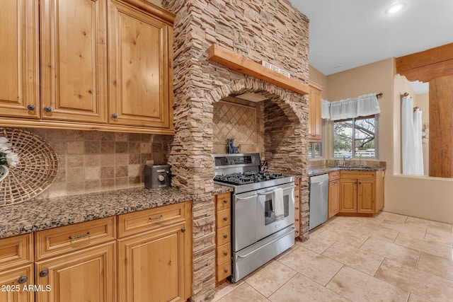 kitchen with sink, backsplash, appliances with stainless steel finishes, and dark stone counters