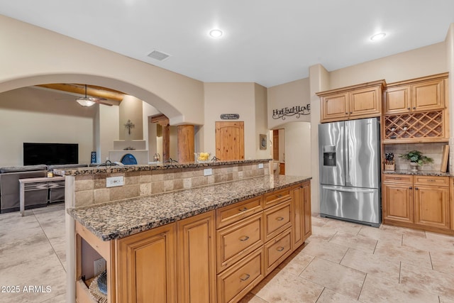 kitchen with a center island, tasteful backsplash, dark stone countertops, stainless steel fridge with ice dispenser, and ceiling fan