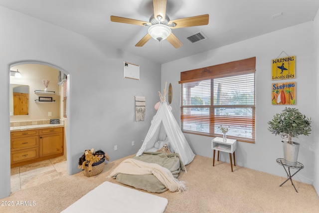 bedroom with ceiling fan, light colored carpet, and ensuite bathroom