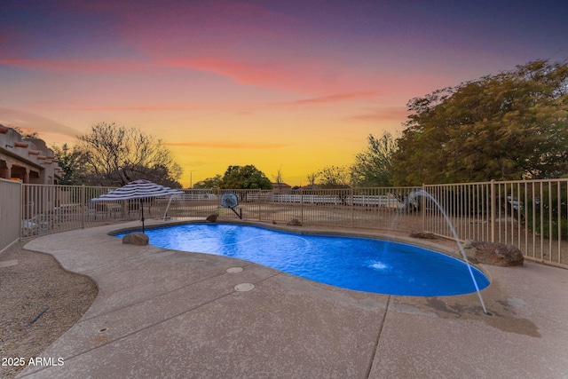 pool at dusk with pool water feature and a patio area