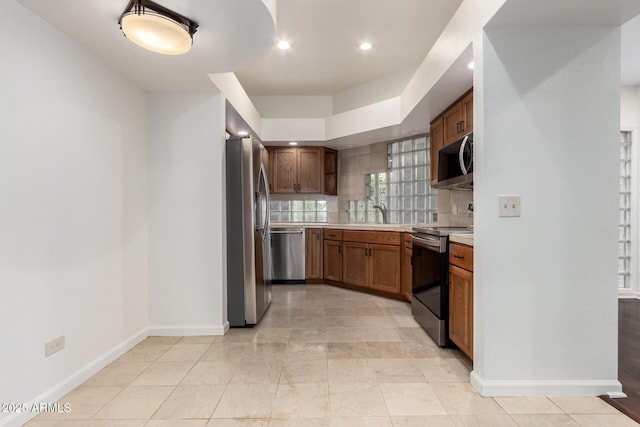 902 W Glendale Ave Unit 102, Phoenix, AZ 85021 - kitchen featuring appliances with stainless steel finishes, light countertops, baseboards, brown cabinetry, and decorative backsplash