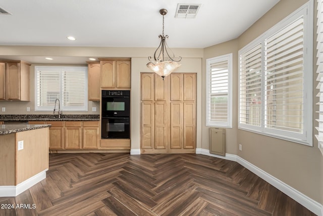 kitchen with light brown cabinets, dark parquet floors, hanging light fixtures, dark stone countertops, and double oven