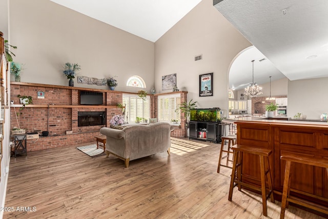 living area featuring high vaulted ceiling, light wood-type flooring, a fireplace, arched walkways, and a chandelier