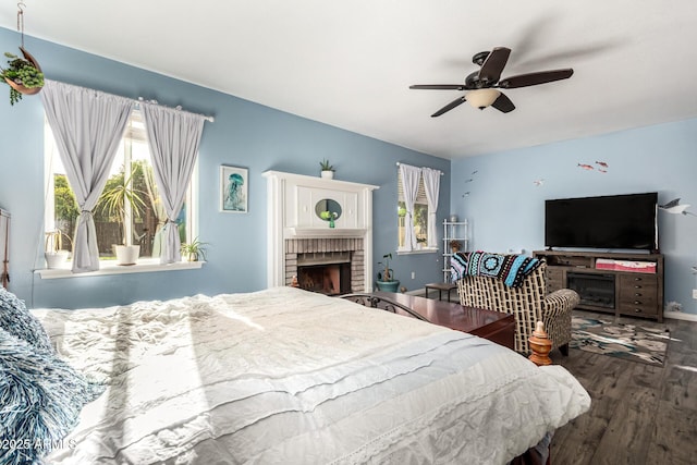 bedroom featuring a brick fireplace, wood finished floors, and a ceiling fan