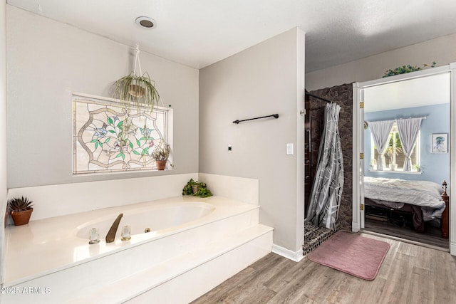ensuite bathroom featuring wood finished floors, a bath, a shower stall, and baseboards