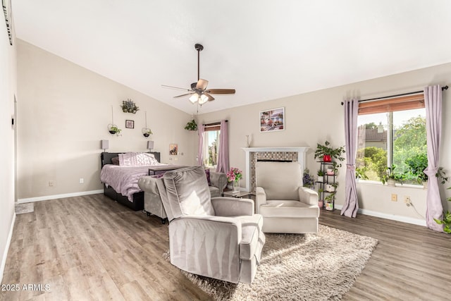 bedroom featuring light wood-type flooring, baseboards, lofted ceiling, a fireplace, and a ceiling fan