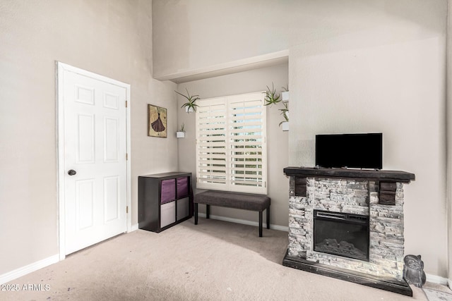 living area featuring carpet floors, baseboards, a stone fireplace, and a high ceiling