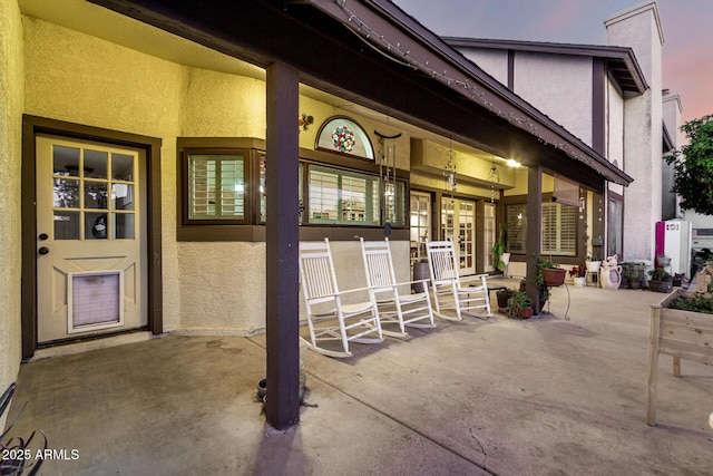 view of exterior entry with stucco siding, covered porch, a chimney, and french doors