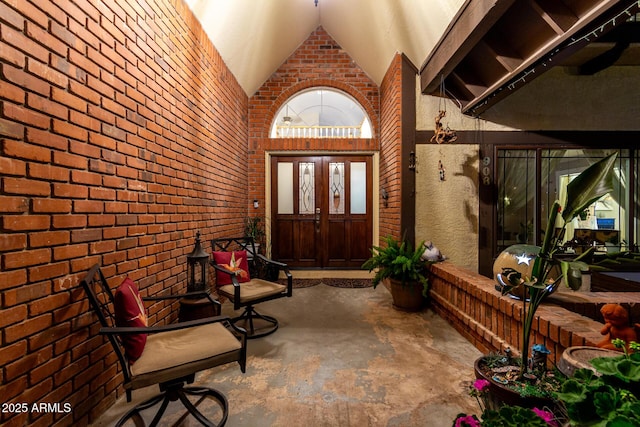 entrance foyer featuring brick wall, unfinished concrete flooring, and high vaulted ceiling