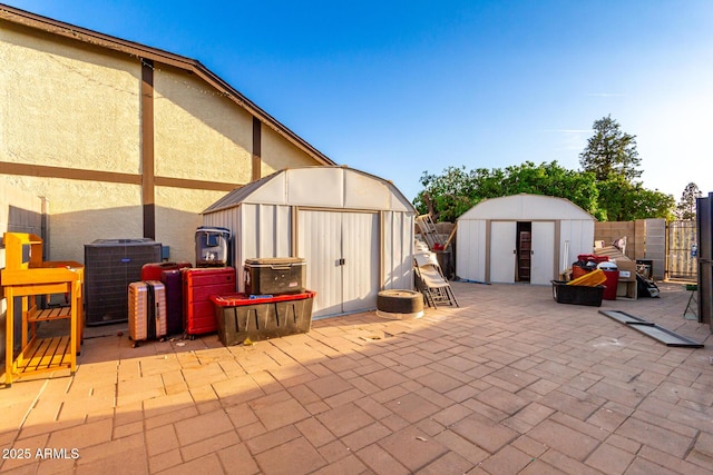 view of patio / terrace with a storage unit, an outbuilding, central AC unit, and fence
