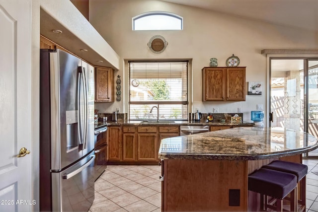 kitchen with a kitchen bar, stainless steel appliances, sink, light tile patterned floors, and lofted ceiling