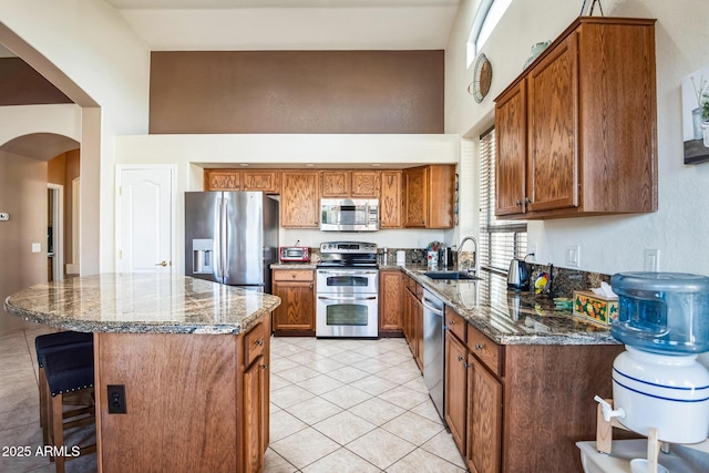 kitchen featuring sink, a center island, dark stone countertops, light tile patterned floors, and appliances with stainless steel finishes